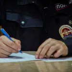 человек в полицейской форме записывает что-то на бумажный лист, руки на столе, лица не видно