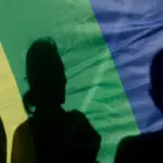 на изобрадении полотно радужного прайд-флага, на котором видны тени нескольких людей
