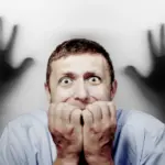 картинка на тему "страх": изображён испуганный мужчина и две тени рук, тянущиеся к нему