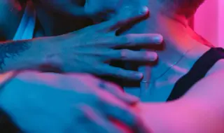 двое мужчин целуются в неоновом освещении, лиц не видно