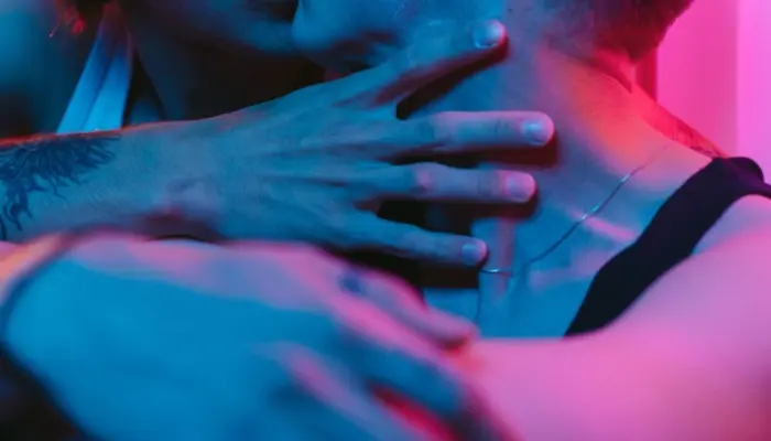 двое мужчин целуются в неоновом освещении, лиц не видно