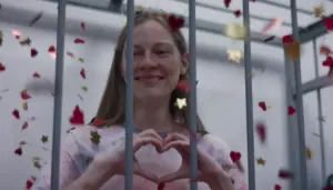 кадр из фильма: главная героиня за решёткой показывает "сердечко" руками