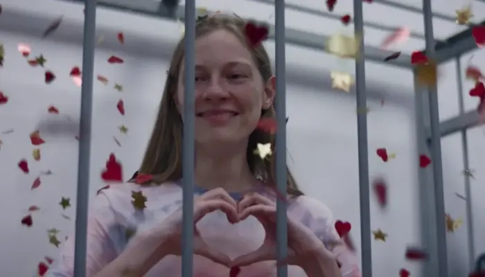 кадр из фильма: главная героиня за решёткой показывает "сердечко" руками