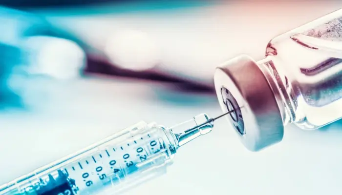 шприц набирает вакцину из колбы